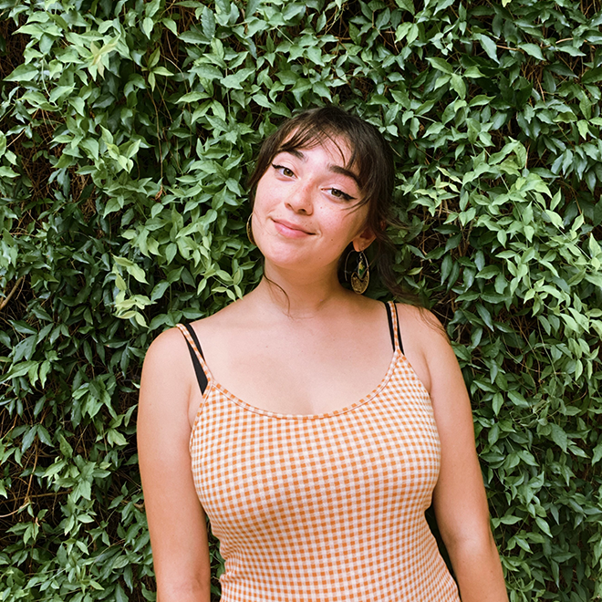 A person smiling in front of green leaves