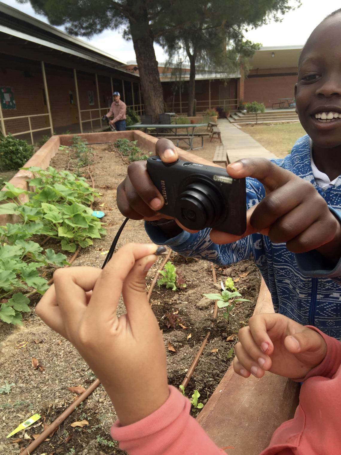 Image of a elementary-aged student taking a photo of a worm that another young student is holding