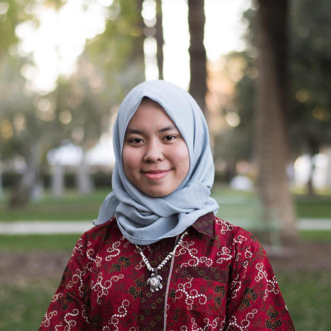 A woman smiling outside wearing a headscarf